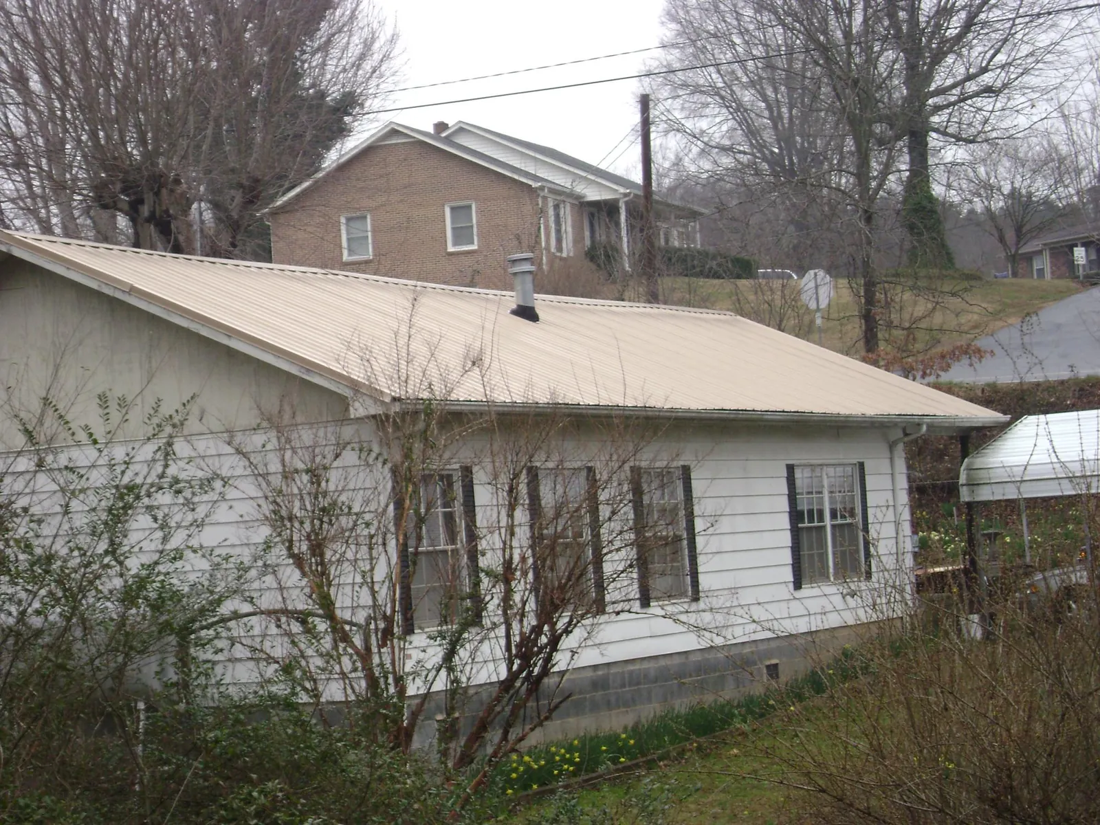 Tan metal roof on a white sided house set into a hillside — Commercial Roofing by Roofing Brothers in Craigsville
